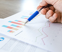 Hand holding pen pointing at charts and graphs